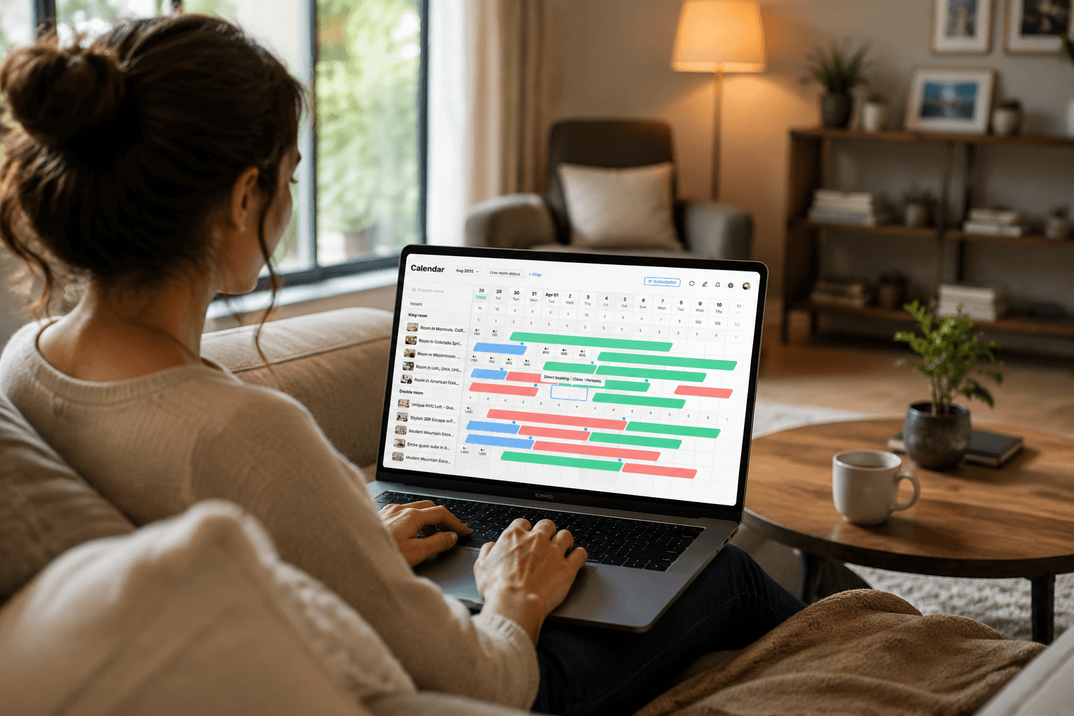 A co-host working from a living room on a laptop, managing Airbnb listings through Hostex team account dashboard with calendar and booking management interface.